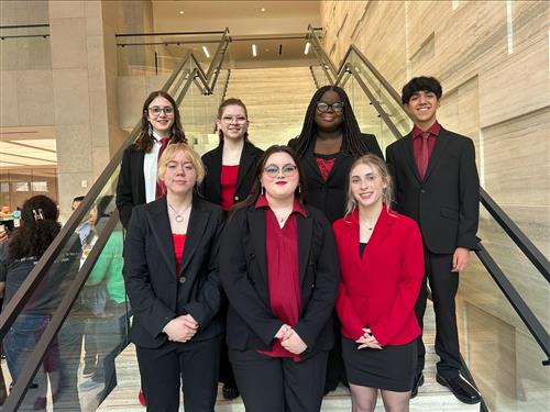 A group of students in business attire stand at the bottom of the stairs